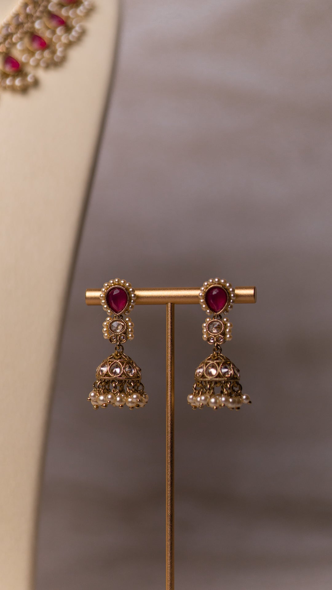 Gold earrings with red gemstones on a stand against a neutral background