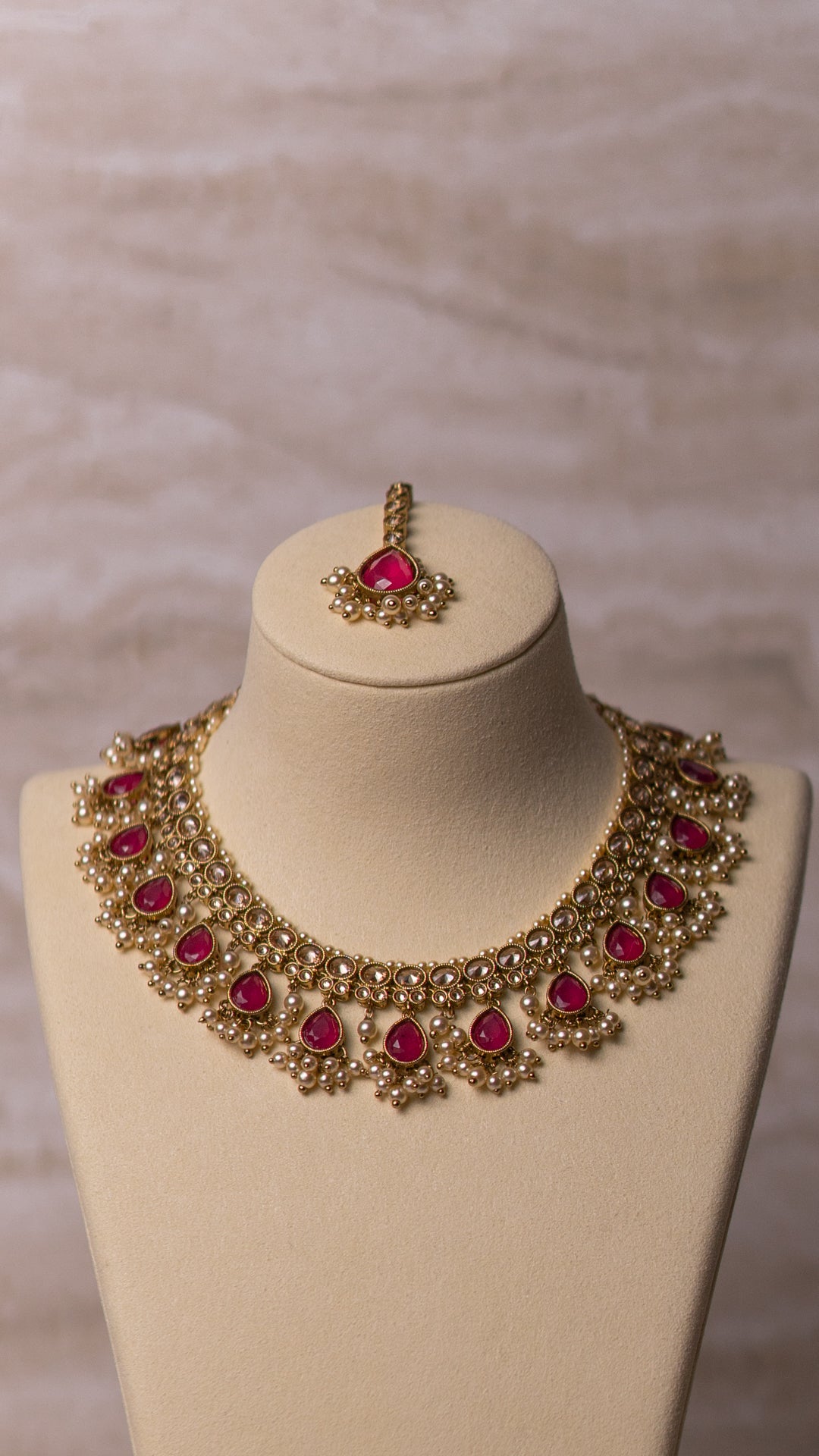 Gold necklace with red stones on a mannequin bust against a neutral background