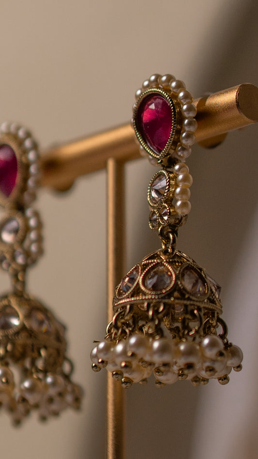 Ornate earrings with red gemstones and pearl-like beads on a stand.