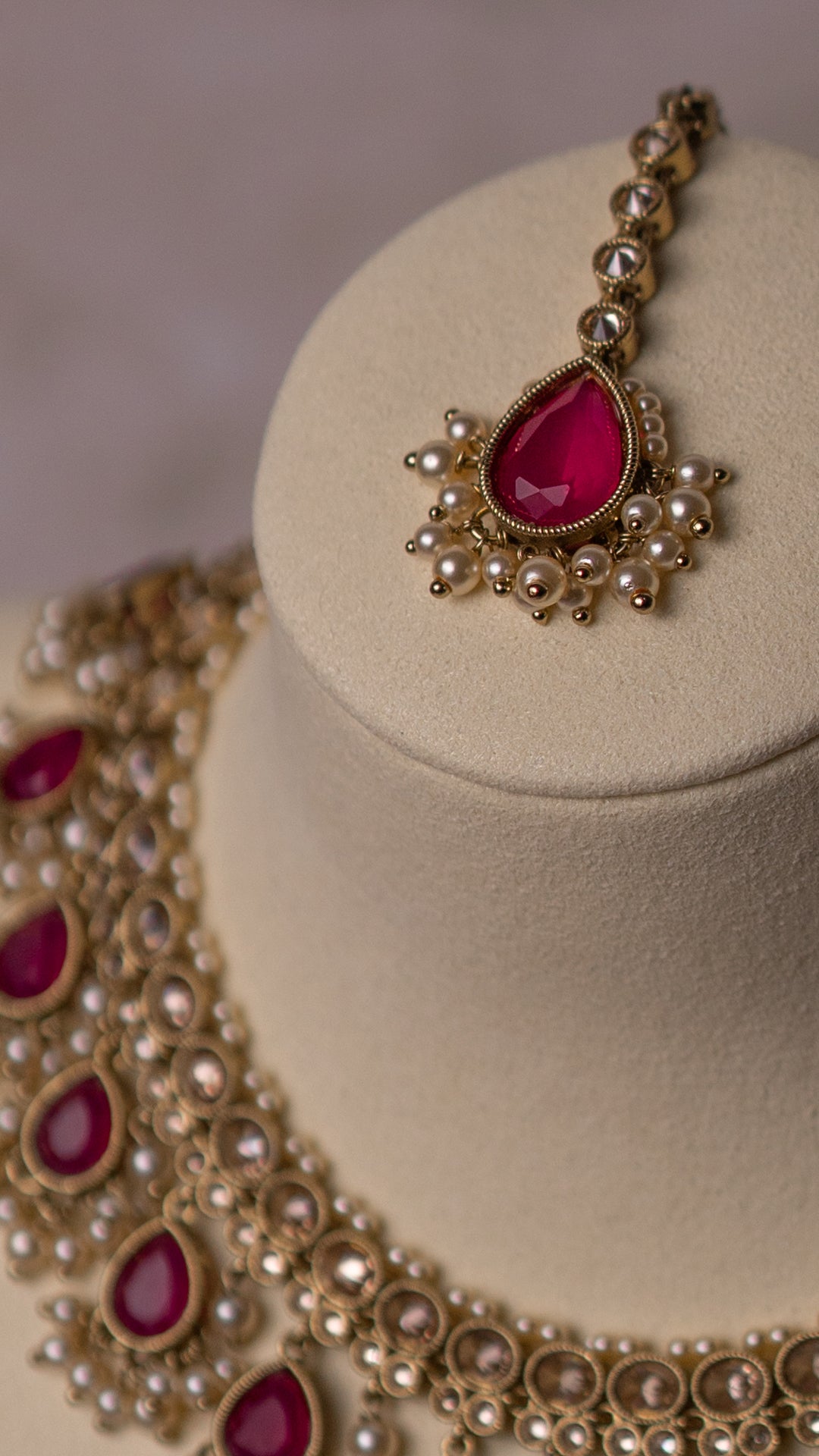 Gold necklace and tikka with red gemstones on a beige stand